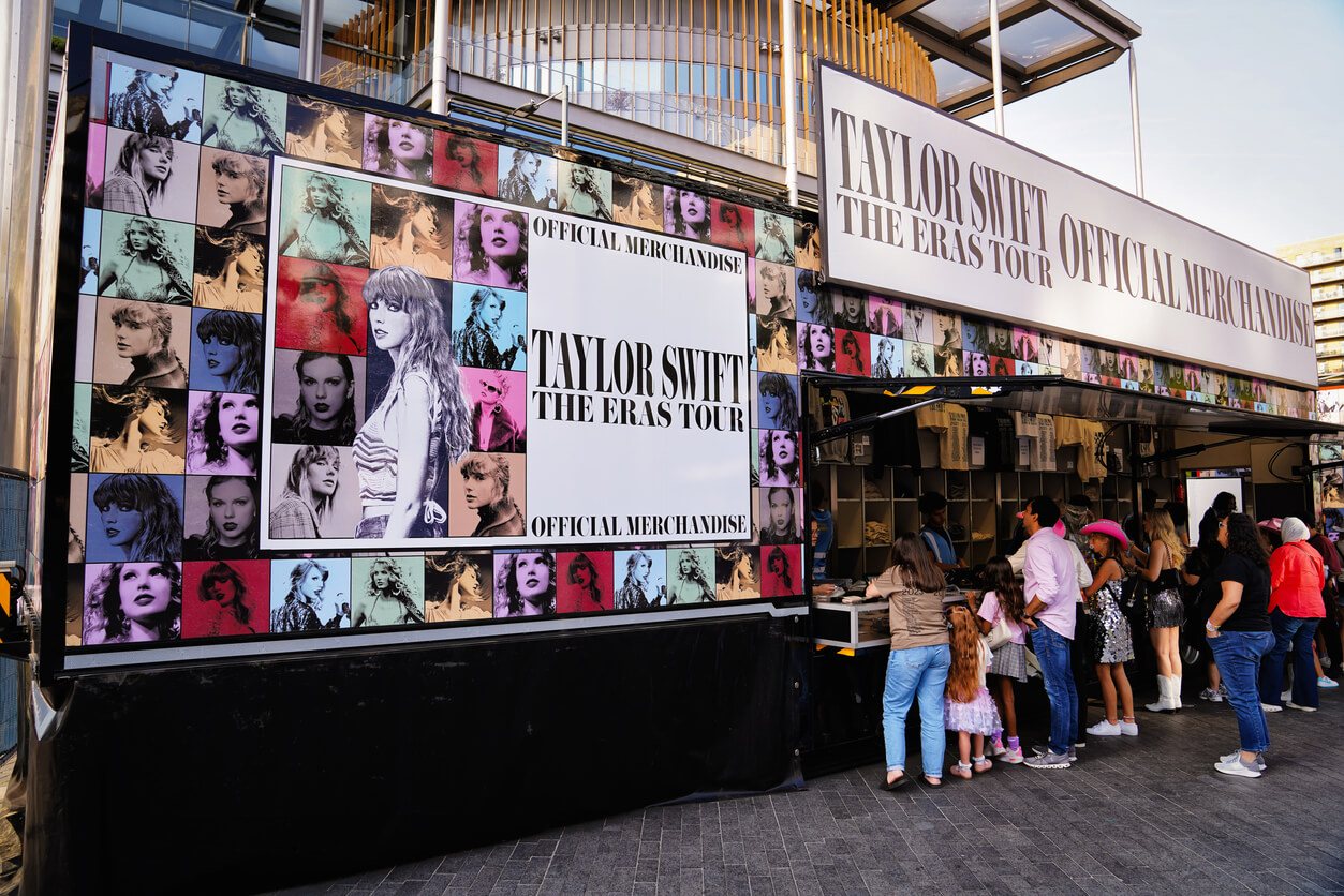 Group of people browsing official merchandise at a Taylor Swift concert. 
