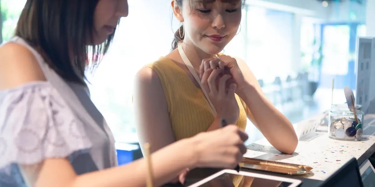 Two customers at a shop counter using a tablet-based point-of-sale system to complete a payment transaction.