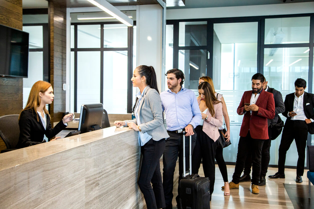 Young woman talking to staff at the front desk of a hotel.