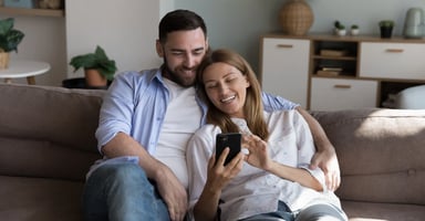 Happy couple using a digital device to make a hotel booking while relaxing at home. 