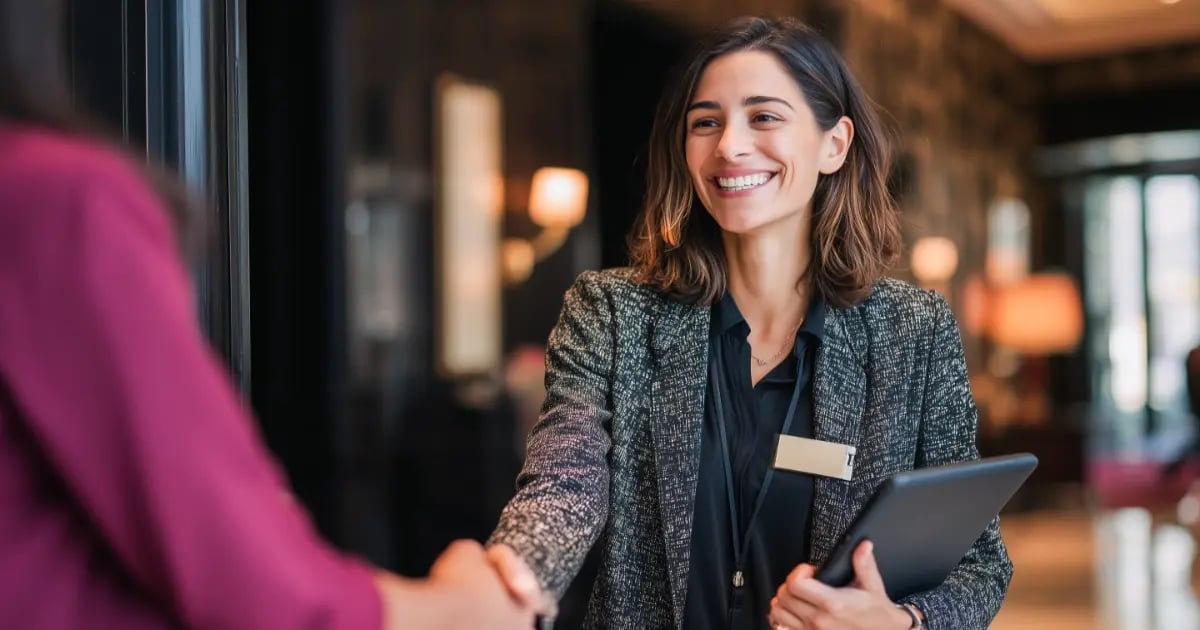 Staff member warmly welcoming a hotel guest while shaking hands.