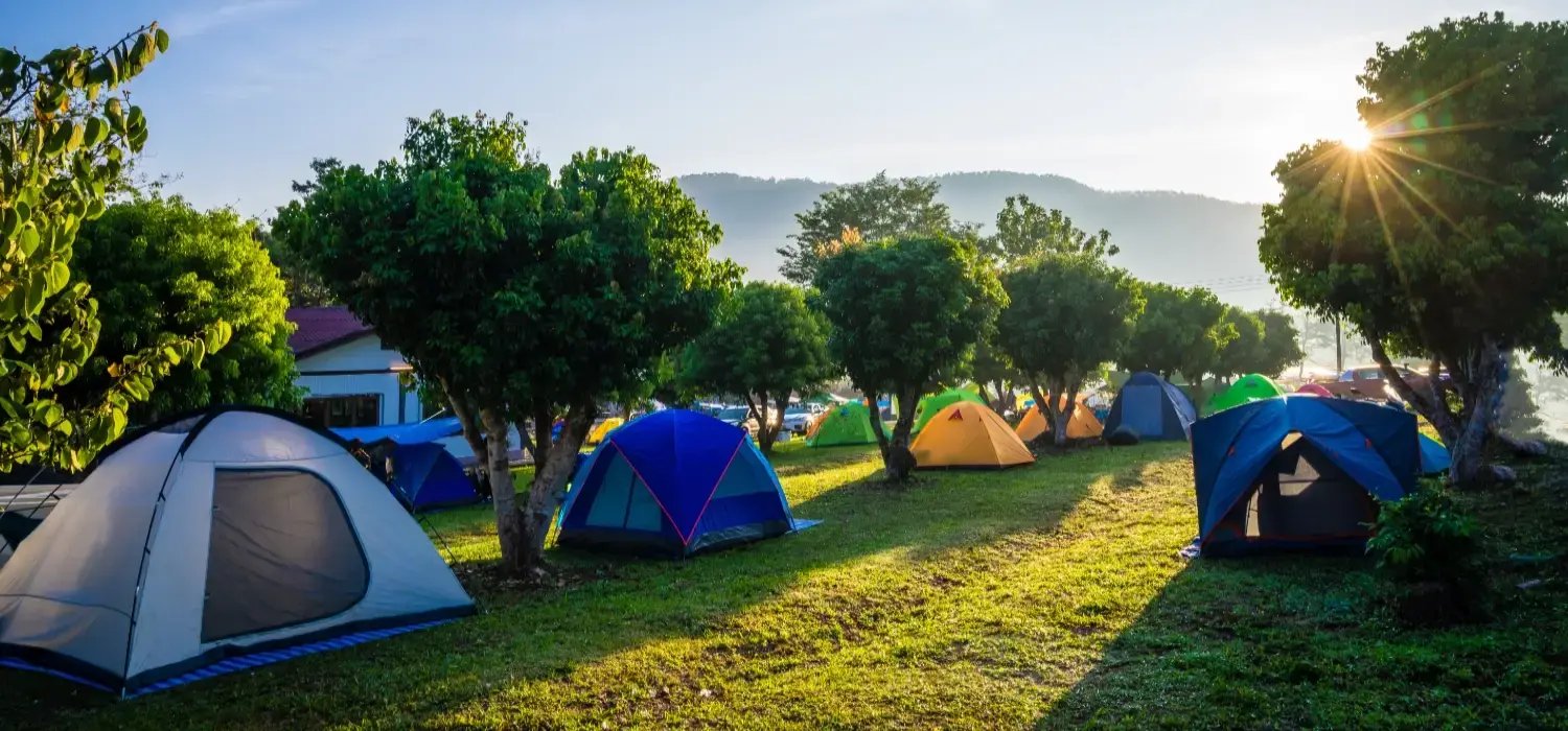Photo showing sunrise over a row of colorful tents in a camping ground.