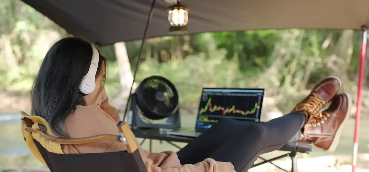 Photo of a woman outdoors reviewing her portfolio performance on a PC.