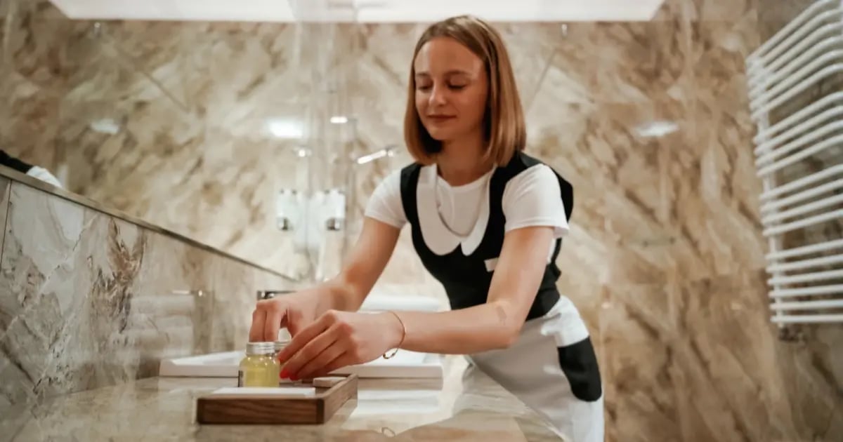 Professional housekeeper carefully cleaning and inspecting hotel guest room, showing attention to detail.