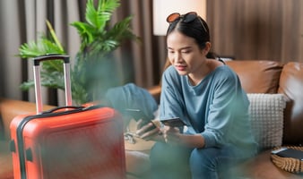 Hotel guest checking booking details on a smartphone beside packed luggage.
