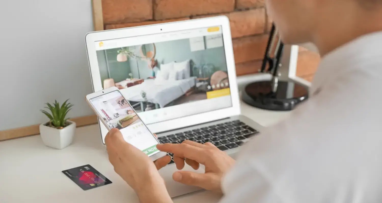 Guest checking hotel room details and prices on a mobile phone while viewing the same property on a laptop.