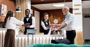 Photo of front desk staff processing guest check-in and payment while another staff member assists a guest. 