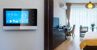 Smart control panel mounted on a wall next to a modern hotel bedroom.
