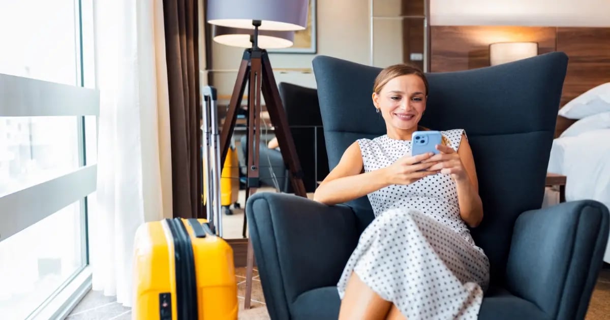 A woman in a hotel room looking at her smartphone, suggesting arrival and in-room comfort.