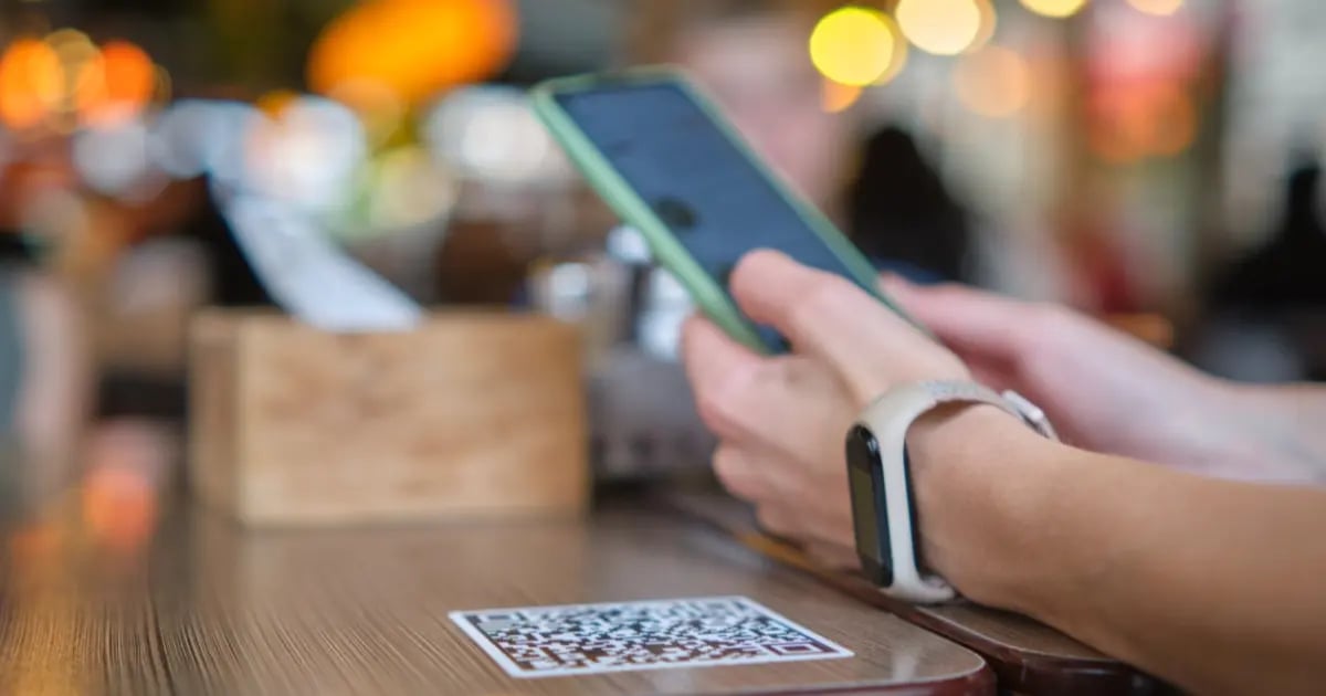 Guest holding a smartphone above a table with a QR code on it, showing the use of technology to streamline guest experience.