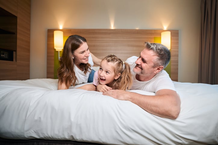Happy caucasian family embracing while lying on bed in hotel room