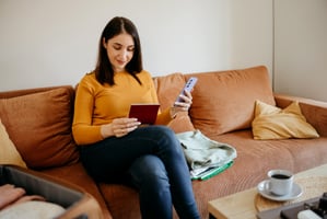 Woman using mobile phone while packing on a sofa